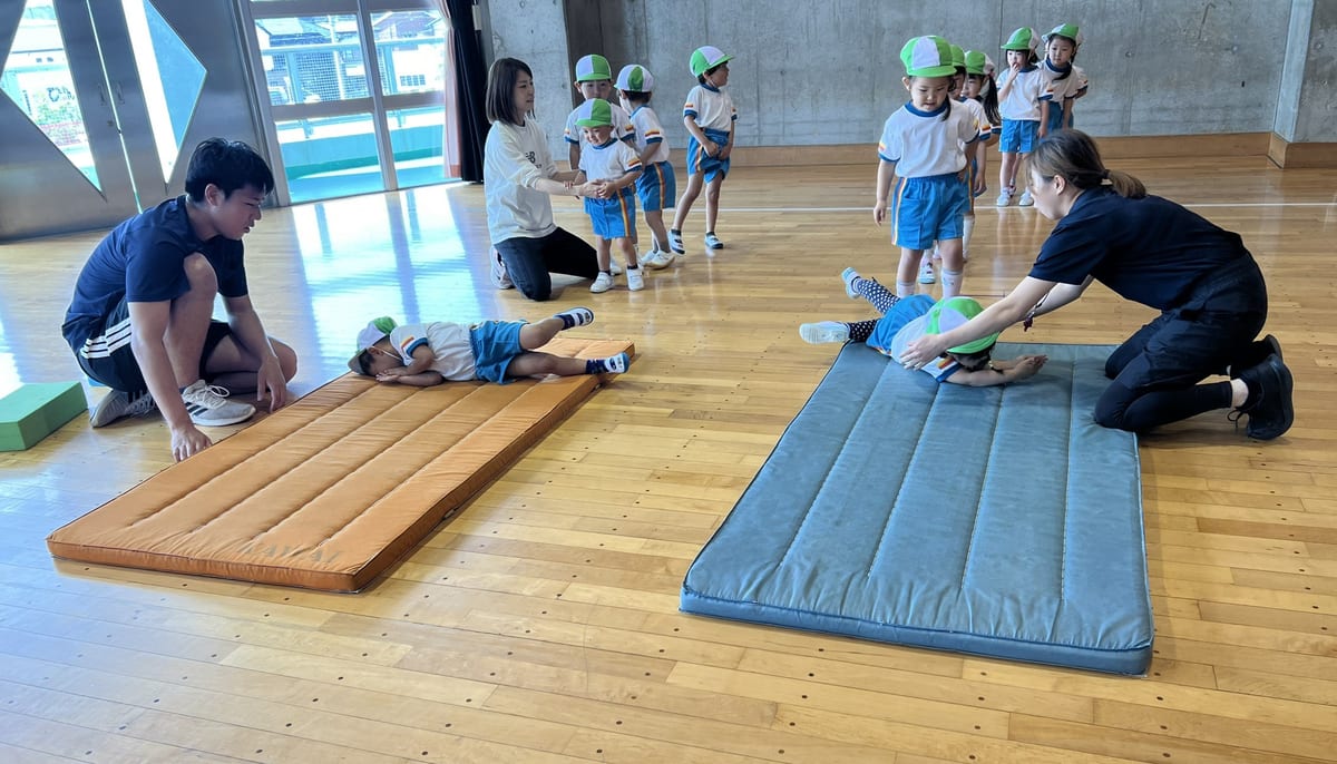 遊戯室で、先生に支えられてマット運動をする子どもたち