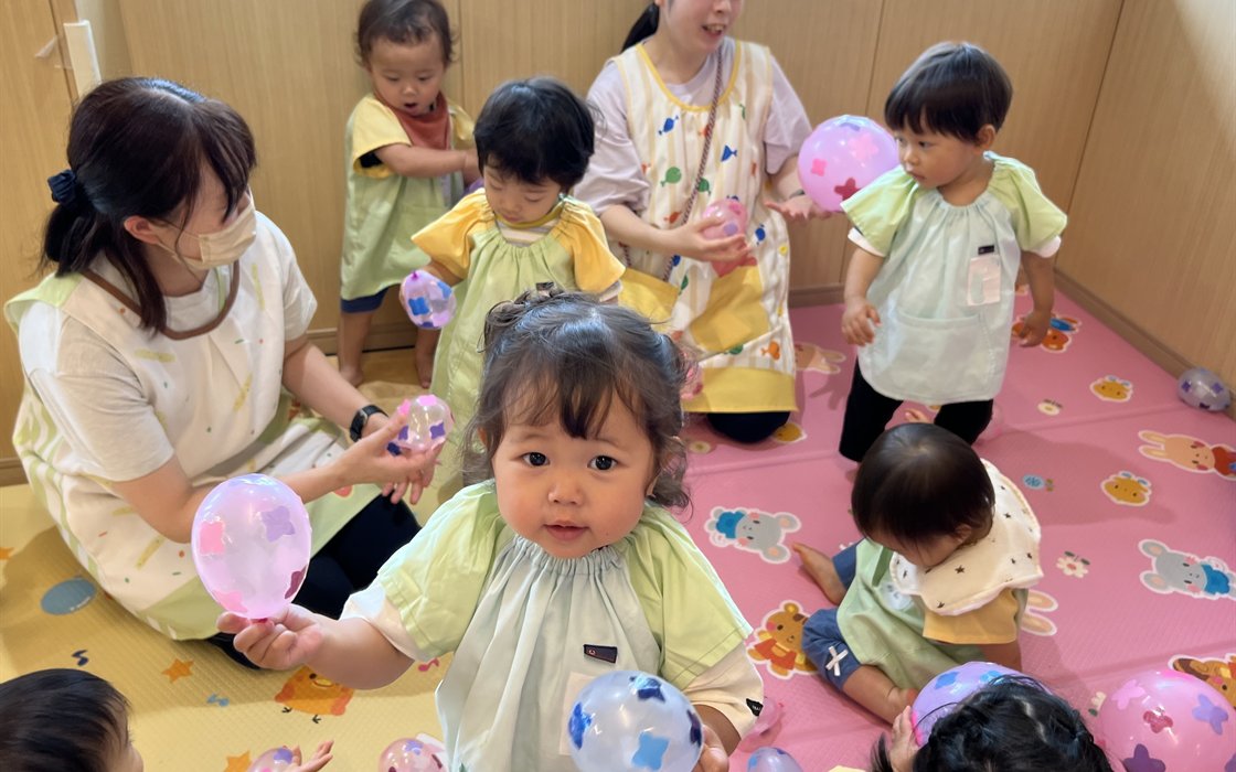 風船を手にのせて遊ぶ子どもたちと保育者
